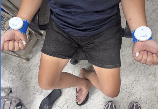 A volunteer sits wearing an electrical stimulator on each wrist